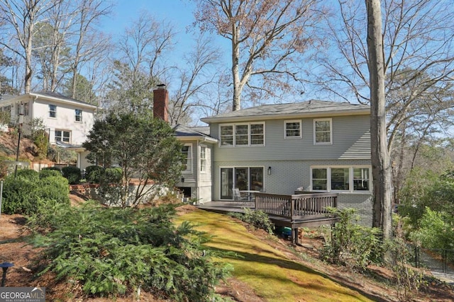 back of property with a wooden deck, brick siding, a chimney, and a lawn