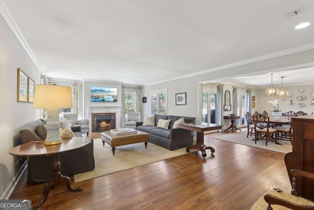 living area featuring crown molding, baseboards, a fireplace, wood finished floors, and a notable chandelier