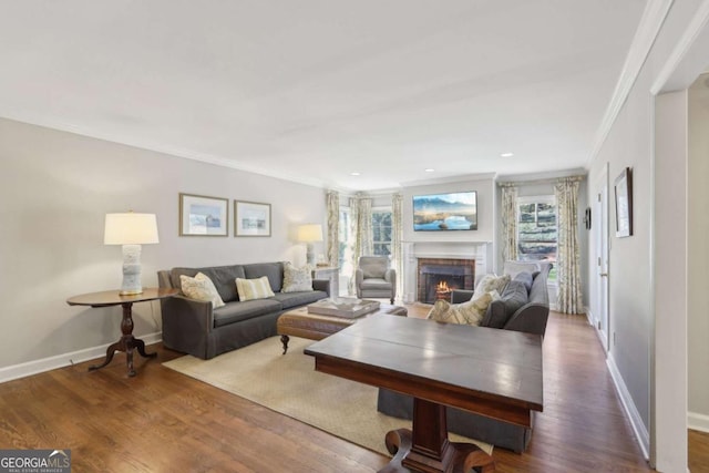 living area featuring baseboards, a warm lit fireplace, ornamental molding, and dark wood-style flooring