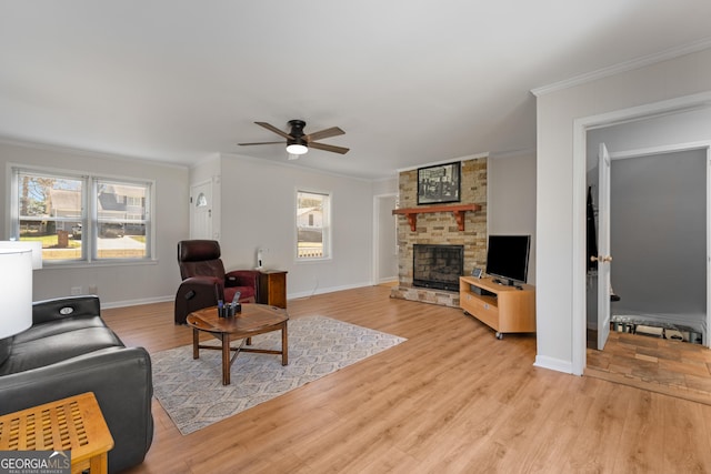 living room with baseboards, ceiling fan, a stone fireplace, crown molding, and light wood-type flooring