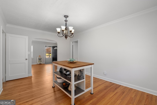 dining area featuring crown molding, baseboards, light wood-style flooring, an inviting chandelier, and arched walkways