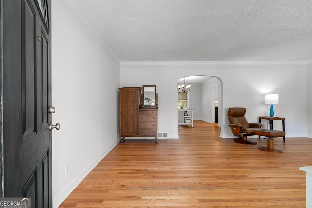 sitting room with visible vents, light wood-style flooring, arched walkways, a textured ceiling, and crown molding