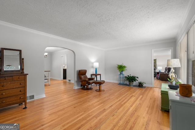 living area featuring crown molding, light wood-style flooring, arched walkways, and a textured ceiling