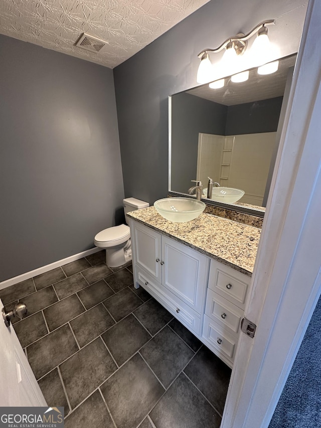 bathroom with a textured ceiling, toilet, vanity, visible vents, and baseboards