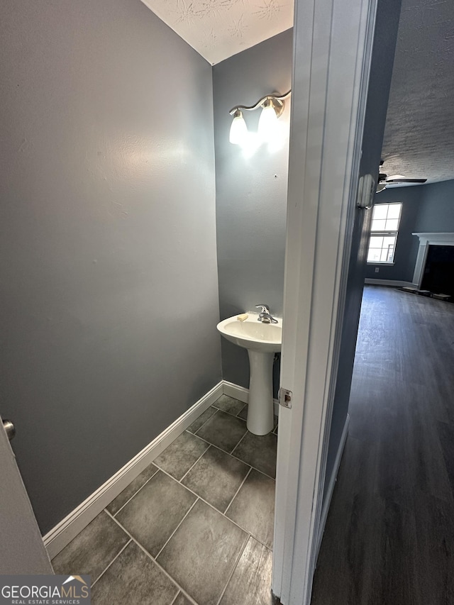 bathroom featuring a ceiling fan, a fireplace, a textured ceiling, and baseboards