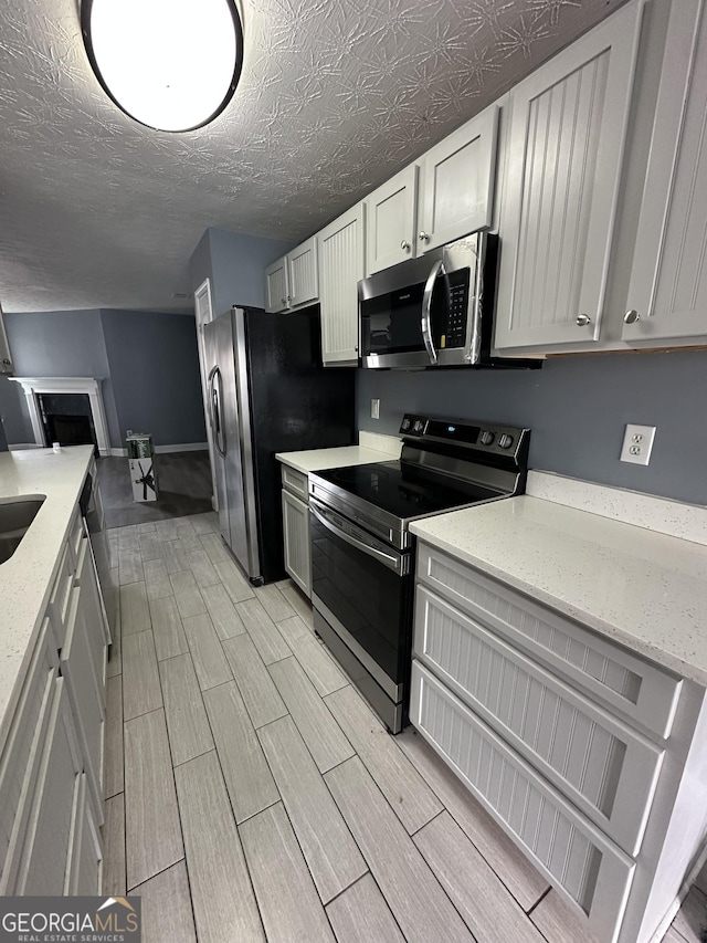 kitchen with baseboards, appliances with stainless steel finishes, light stone countertops, a textured ceiling, and wood finish floors