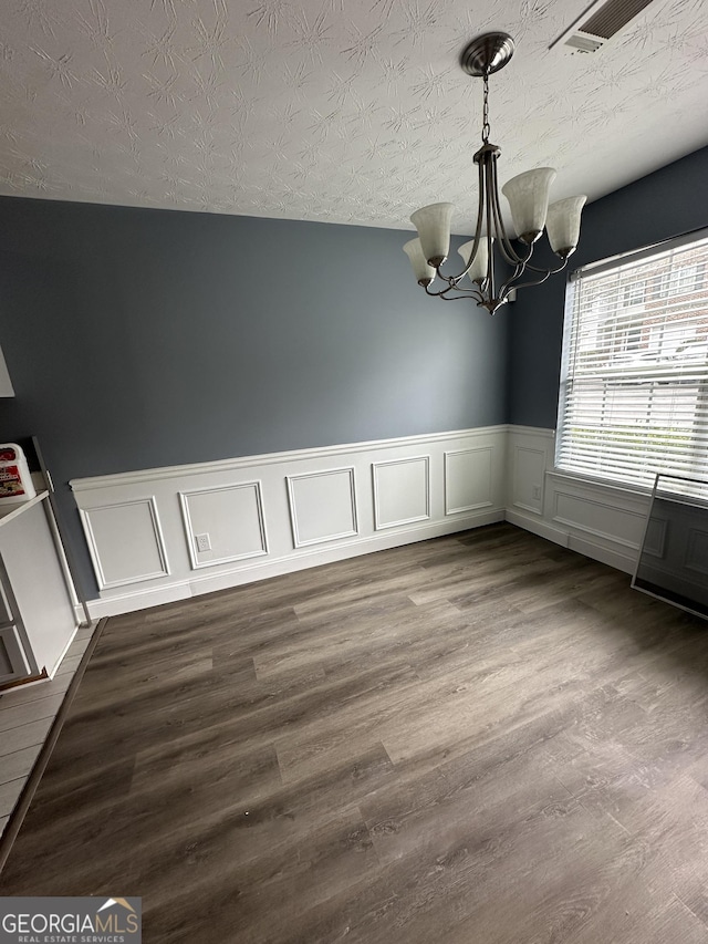 unfurnished dining area featuring a textured ceiling, dark wood-type flooring, visible vents, and a notable chandelier