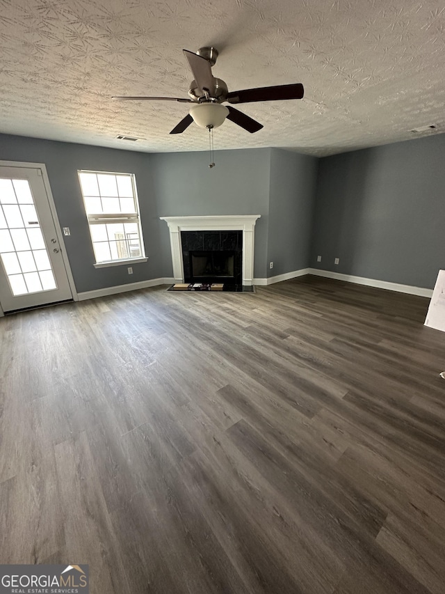 unfurnished living room featuring dark wood-style flooring, visible vents, a tiled fireplace, a textured ceiling, and baseboards