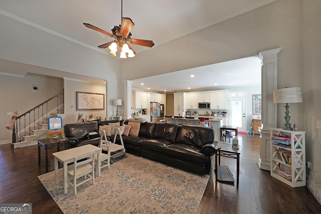 living room featuring stairs, ornamental molding, decorative columns, a ceiling fan, and dark wood-style flooring