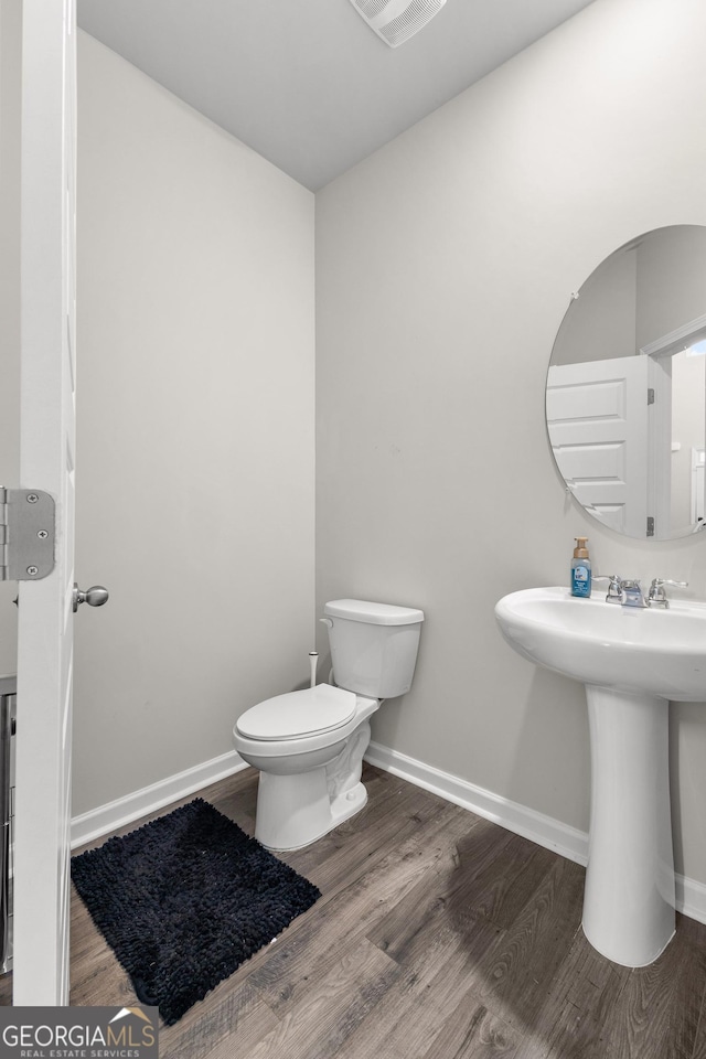 bathroom featuring toilet, a sink, visible vents, wood finished floors, and baseboards