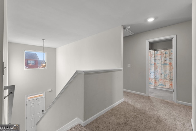 hall featuring baseboards, carpet flooring, a notable chandelier, and an upstairs landing