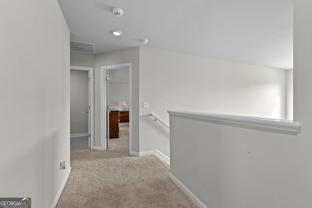 corridor with carpet floors, baseboards, visible vents, and an upstairs landing