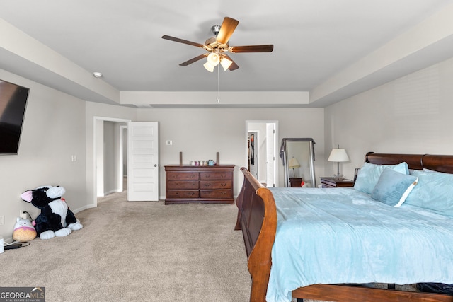 carpeted bedroom featuring baseboards, a tray ceiling, a walk in closet, and a ceiling fan