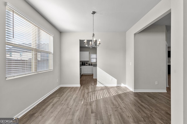 unfurnished dining area with a chandelier, wood finished floors, and baseboards