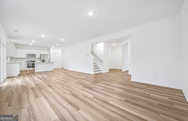 unfurnished living room featuring baseboards, light wood finished floors, stairway, and recessed lighting