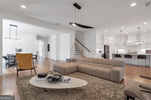 living room featuring light wood-type flooring, arched walkways, stairway, and recessed lighting