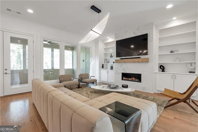 living room featuring built in features, crown molding, light wood finished floors, visible vents, and a premium fireplace