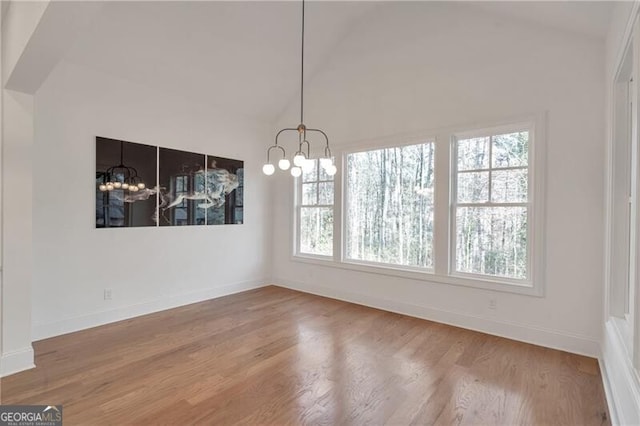 unfurnished dining area with vaulted ceiling, baseboards, wood finished floors, and an inviting chandelier