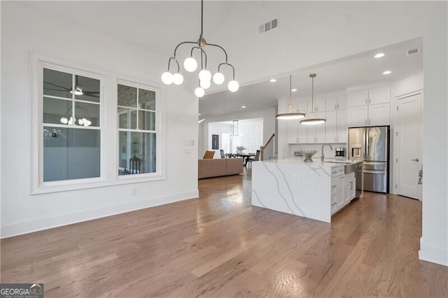 kitchen with stainless steel fridge, visible vents, white cabinets, open floor plan, and a notable chandelier