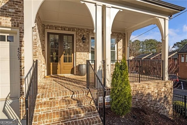 entrance to property featuring an attached garage, french doors, and brick siding