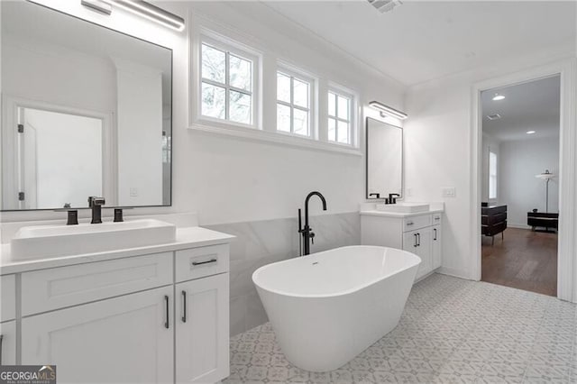 full bath with a freestanding bath, two vanities, a sink, and visible vents