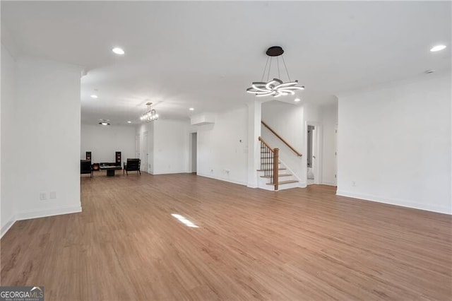 unfurnished living room with light wood-style flooring, recessed lighting, a notable chandelier, and stairway