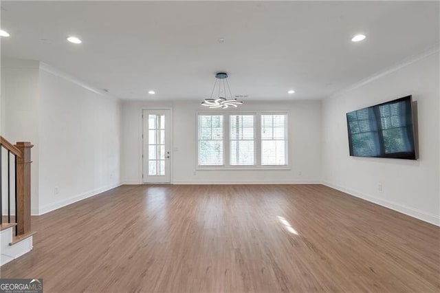 unfurnished living room featuring a chandelier, stairway, baseboards, and wood finished floors