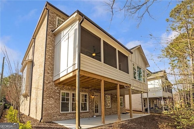 rear view of property featuring brick siding, board and batten siding, a patio area, and a sunroom