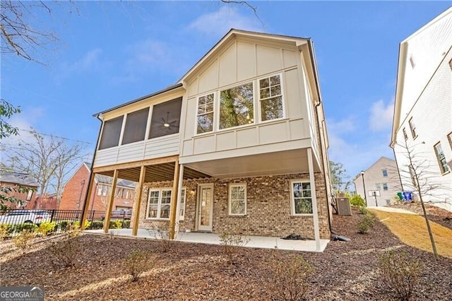 rear view of house with a sunroom, fence, central air condition unit, board and batten siding, and brick siding