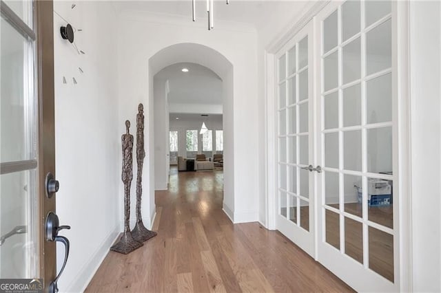 corridor with arched walkways, french doors, crown molding, wood finished floors, and baseboards