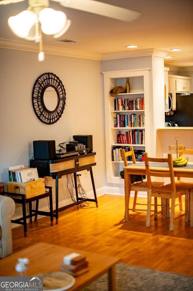 living area with light wood-type flooring, visible vents, and ornamental molding