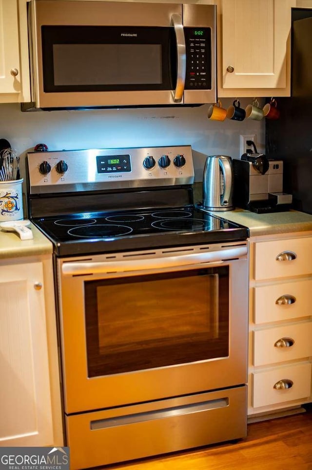 kitchen featuring appliances with stainless steel finishes, white cabinets, light countertops, and wood finished floors