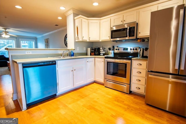 kitchen with light wood finished floors, appliances with stainless steel finishes, ornamental molding, a sink, and a peninsula