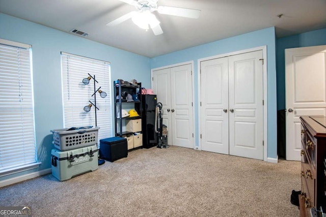 interior space with light carpet, two closets, visible vents, and a ceiling fan