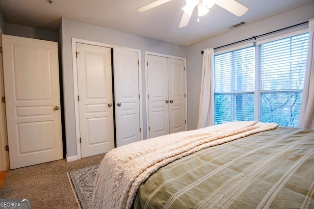 bedroom with a ceiling fan, visible vents, multiple closets, and carpet flooring