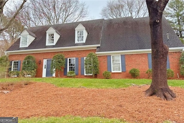 cape cod-style house featuring a shingled roof, a front yard, and brick siding