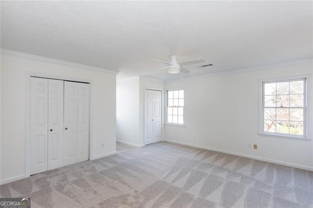 unfurnished bedroom with multiple closets, light carpet, ornamental molding, and baseboards