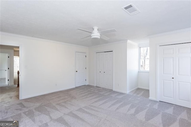 unfurnished bedroom featuring light carpet, crown molding, visible vents, and two closets