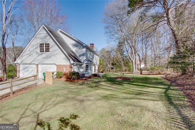 view of side of home featuring a garage, brick siding, fence, a yard, and a chimney