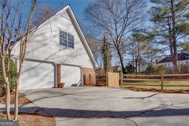 view of home's exterior with driveway, a garage, fence, and brick siding