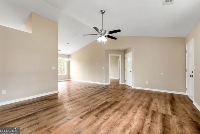 unfurnished living room with ceiling fan with notable chandelier, vaulted ceiling, wood finished floors, and baseboards