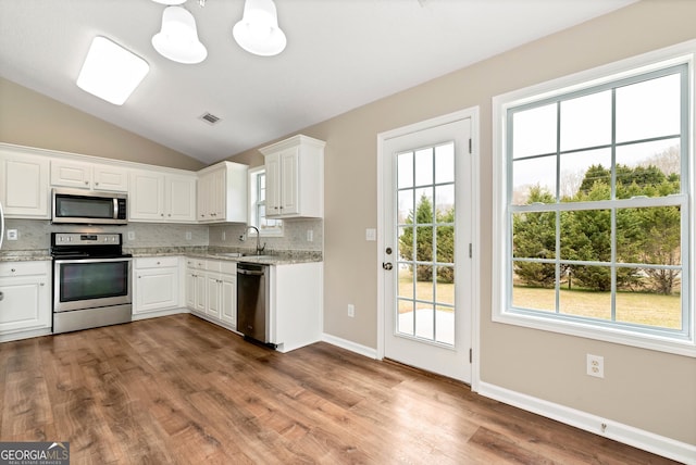 kitchen featuring visible vents, decorative backsplash, lofted ceiling, stainless steel appliances, and a sink