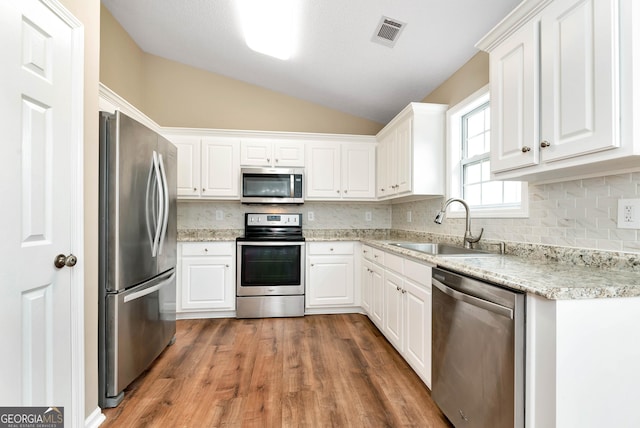 kitchen featuring visible vents, lofted ceiling, appliances with stainless steel finishes, white cabinetry, and a sink