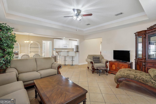 living area featuring light tile patterned floors, visible vents, a tray ceiling, crown molding, and ceiling fan with notable chandelier