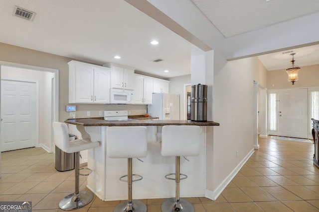 kitchen with light tile patterned floors, white appliances, a kitchen bar, and visible vents