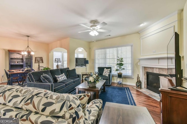 living area featuring ceiling fan with notable chandelier, plenty of natural light, a tiled fireplace, and wood finished floors