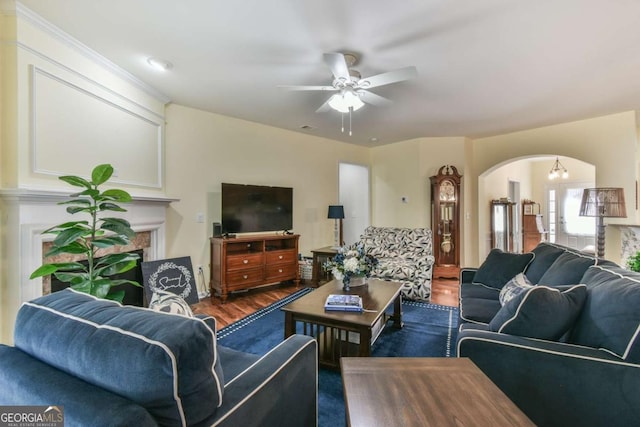 living room featuring a ceiling fan, arched walkways, dark wood-style flooring, and a fireplace