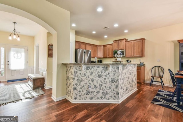 kitchen featuring arched walkways, light stone counters, brown cabinets, dark wood-type flooring, and stainless steel appliances