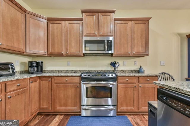 kitchen with stainless steel appliances, light stone counters, and wood finished floors