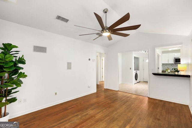 unfurnished living room featuring lofted ceiling, visible vents, a ceiling fan, wood finished floors, and washer / dryer